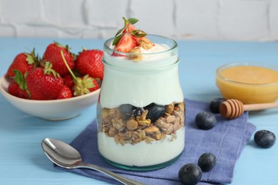 Photo of Tasty yogurt with granola, berries, honey and spoon on light blue wooden table, closeup