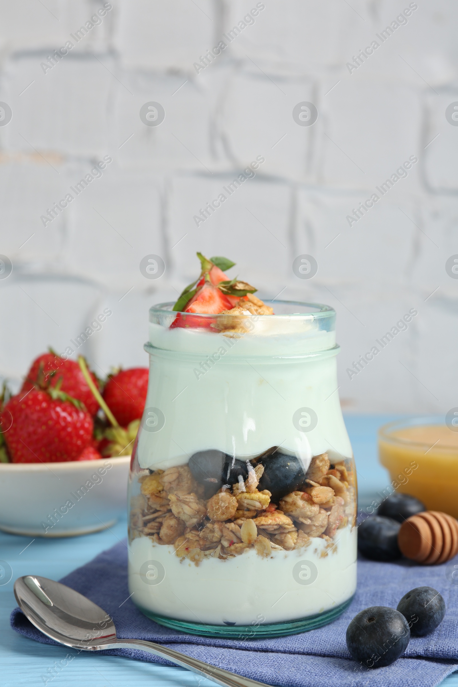 Photo of Tasty yogurt with granola, berries, honey and spoon on light blue table, closeup