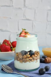 Photo of Tasty yogurt with granola, berries, honey and spoon on light blue table, closeup