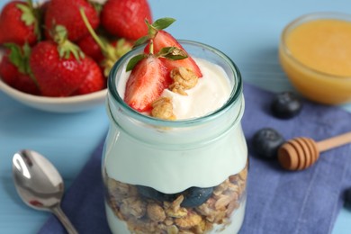 Photo of Tasty yogurt with granola, berries and honey on light blue table, closeup