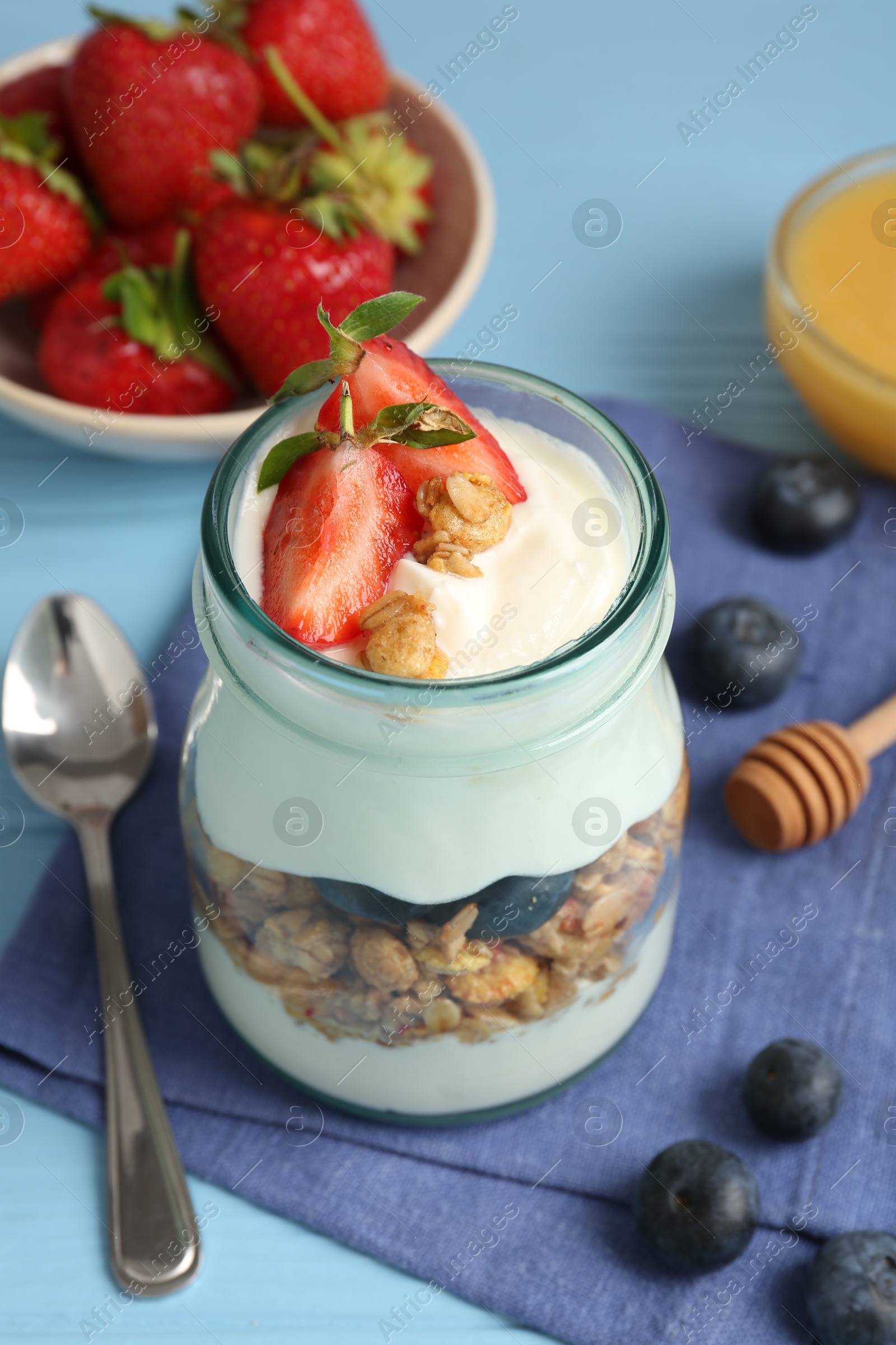Photo of Tasty yogurt with granola, berries and honey on light blue wooden table, closeup