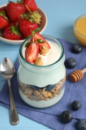 Photo of Tasty yogurt with granola, berries and honey on light blue wooden table, closeup