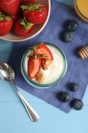 Photo of Tasty yogurt with granola, berries and spoon on light blue wooden table, flat lay