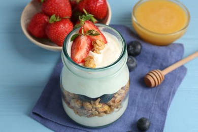 Photo of Tasty yogurt with granola, berries and honey on light blue wooden table, closeup