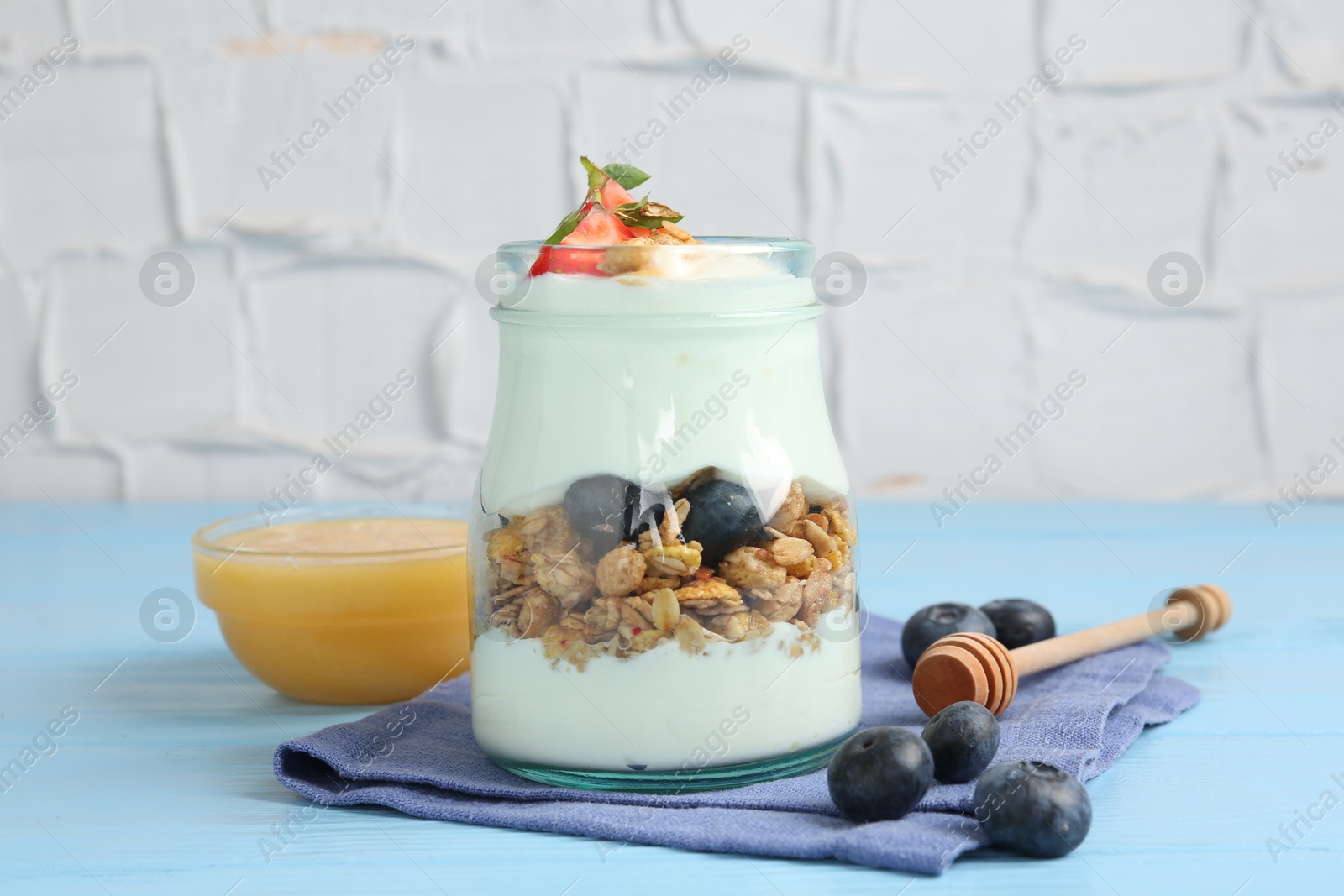 Tasty yogurt with granola, berries and honey on light blue wooden table, closeup Photo of Tasty yogurt with granola, berries and honey on light blue wooden table, closeup