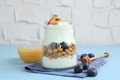 Photo of Tasty yogurt with granola, berries and honey on light blue wooden table, closeup