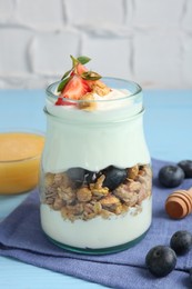 Photo of Tasty yogurt with granola, berries and honey on light blue table, closeup