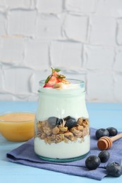Photo of Tasty yogurt with granola, berries and honey on light blue wooden table, closeup