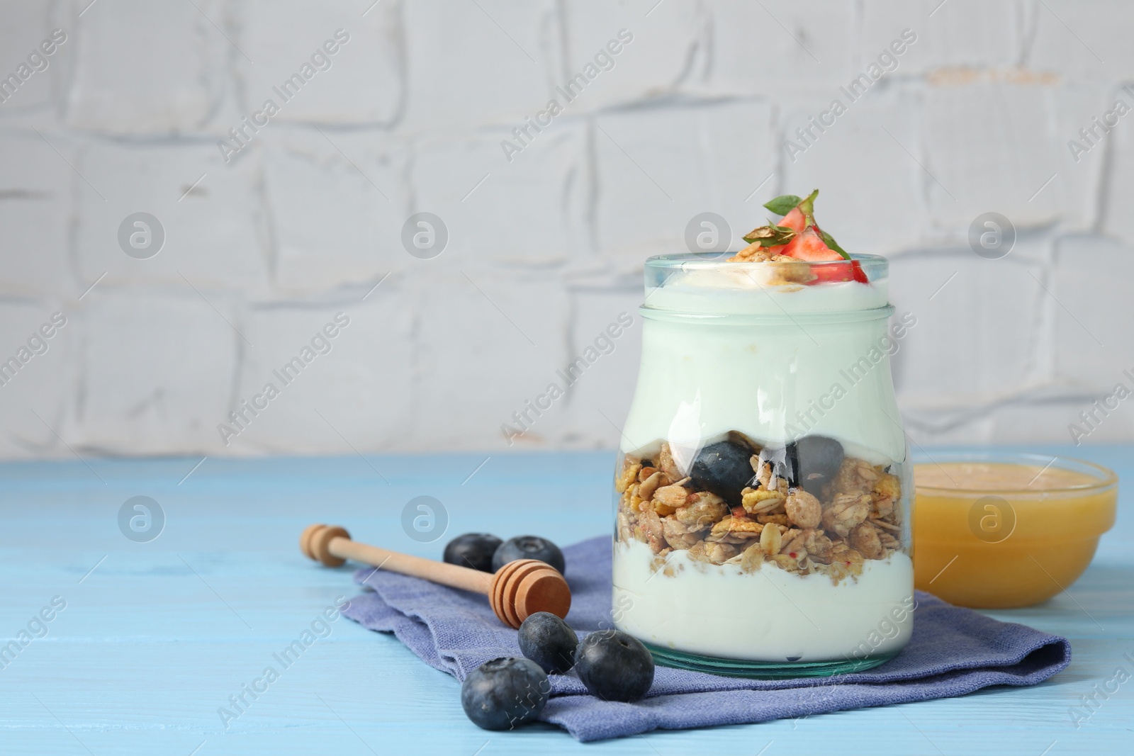 Photo of Tasty yogurt with granola, berries and honey on light blue wooden table, closeup. Space for text