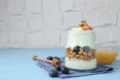 Photo of Tasty yogurt with granola, berries and honey on light blue wooden table, closeup. Space for text