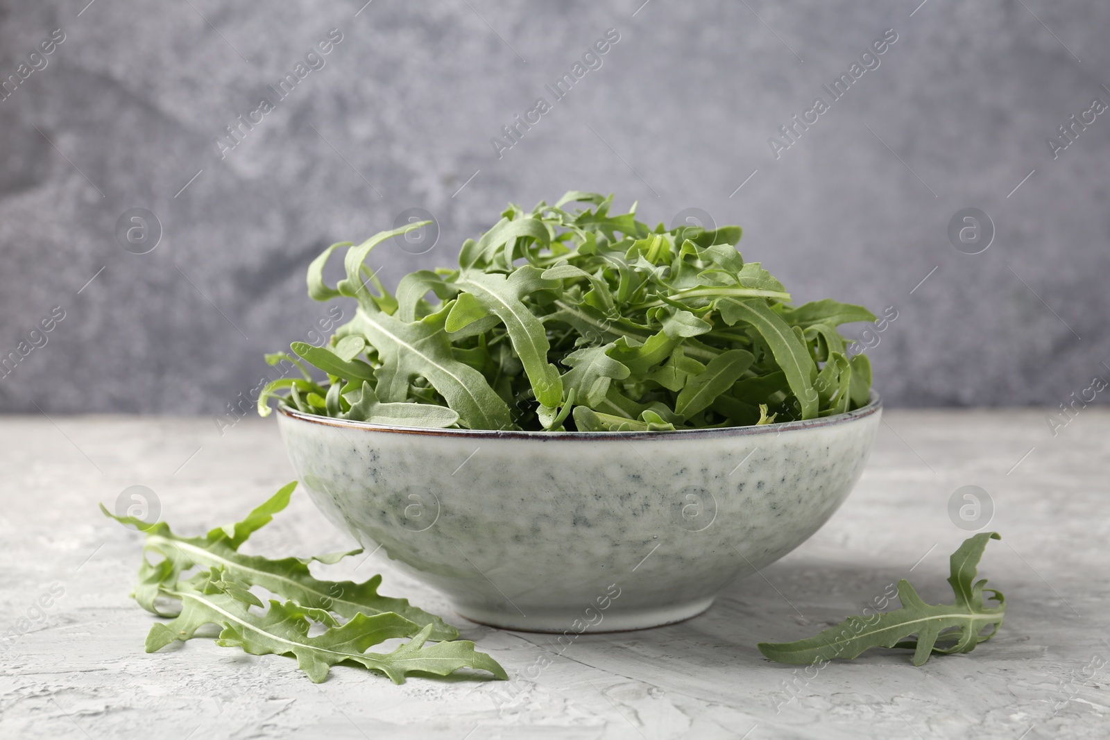 Photo of Fresh ripe green arugula leaves in bowl on grey table, closeup
