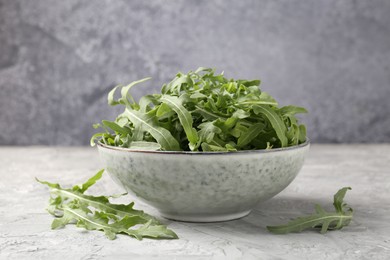 Photo of Fresh ripe green arugula leaves in bowl on grey table, closeup