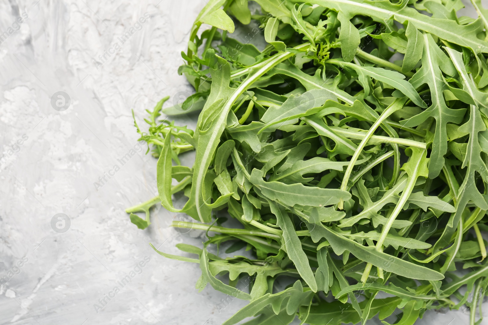 Fresh ripe green arugula leaves on grey table, top view. Space for text Photo of Fresh ripe green arugula leaves on grey table, top view. Space for text