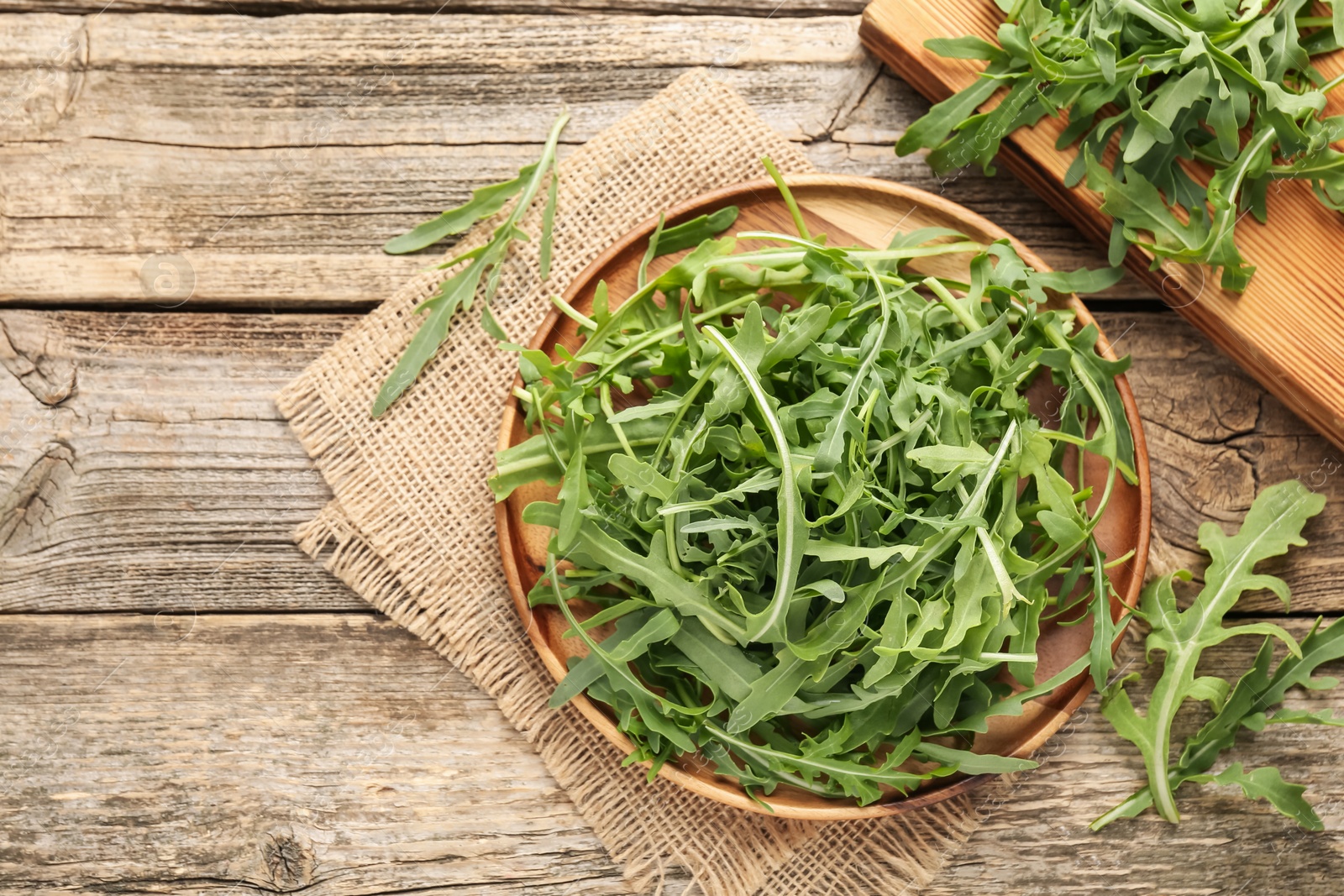 Photo of Fresh ripe green arugula leaves on wooden table, flat lay. Space for text