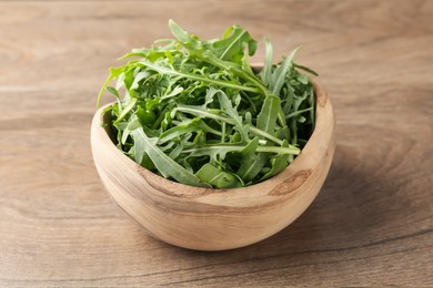Photo of Fresh ripe green arugula leaves in bowl on wooden table, closeup