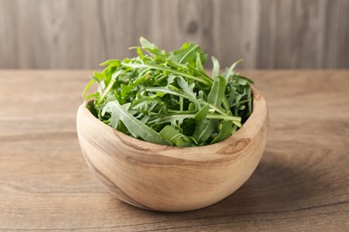 Photo of Fresh ripe green arugula leaves in bowl on wooden table, closeup