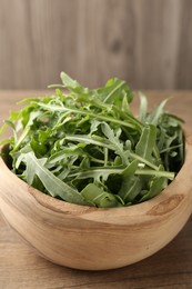 Photo of Fresh ripe green arugula leaves in bowl on wooden table, closeup