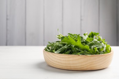 Photo of Fresh ripe green arugula leaves on white wooden table, closeup. Space for text