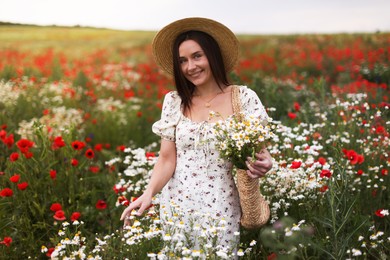 Photo of Smiling woman in hat with bag of chamomile flowers in wildflower meadow