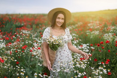 Photo of Smiling woman in hat with bag of chamomile flowers in wildflower meadow