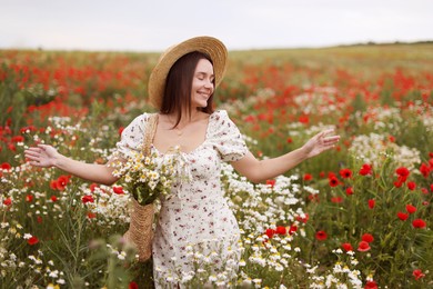 Photo of Smiling woman in hat with bag of chamomile flowers enjoying nature in wildflower meadow