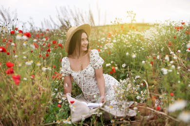 Photo of Smiling woman in hat reading book in wildflower meadow