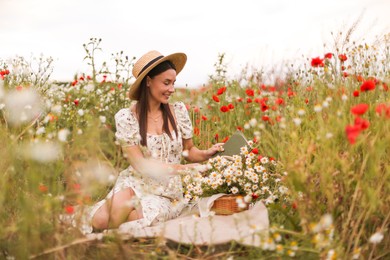 Photo of Smiling woman in hat with book and basket of chamomile flowers in wildflower meadow