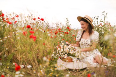 Photo of Smiling woman in hat with book and basket of chamomile flowers in wildflower meadow