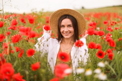 Photo of Smiling woman in hat among red poppy flowers in wildflower meadow