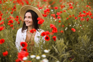 Photo of Smiling woman in hat among red poppy flowers in wildflower meadow