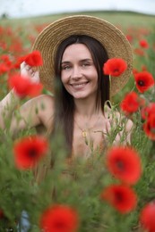 Photo of Portrait of smiling woman in hat among red poppy flowers in wildflower meadow