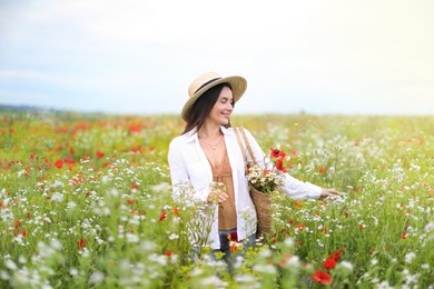Photo of Smiling woman in hat with bag of flowers walking in wildflower meadow