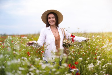 Photo of Smiling woman in hat with bag of flowers walking in wildflower meadow