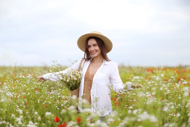 Photo of Smiling woman in hat with bag of chamomile flowers walking in wildflower meadow