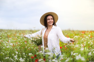 Photo of Smiling woman in hat with bag of chamomile flowers walking in wildflower meadow