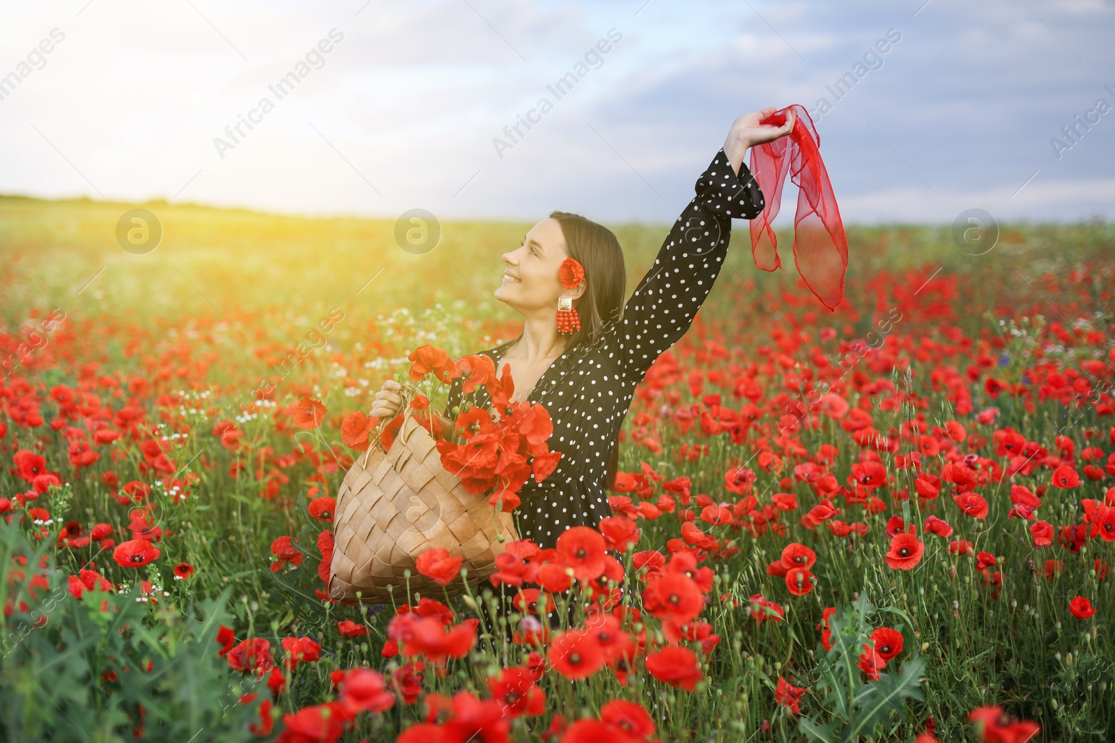 Photo of Smiling woman with bag and handkerchief among red poppy flowers in morning wildflower meadow