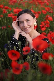 Photo of Portrait of smiling woman among red poppy flowers in wildflower meadow