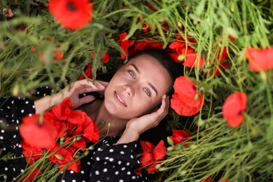 Photo of Portrait of smiling woman among red poppy flowers in wildflower meadow, top view