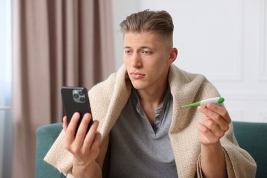Photo of Man with thermometer having online consultation with doctor via smartphone at home