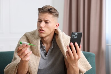 Photo of Man with thermometer having online consultation with doctor via smartphone at home