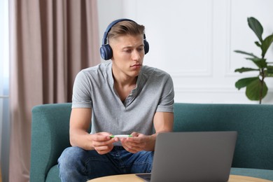 Photo of Man in headphones with thermometer having online consultation with doctor via laptop at home