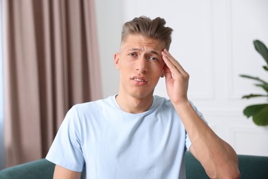 Photo of Sad man suffering from headache at home. Online medical consultation