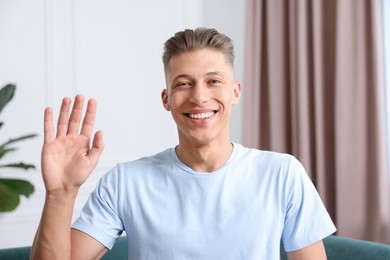 Photo of Portrait of happy man waving at home. Online medical consultation