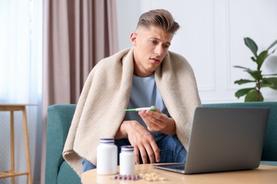 Photo of Sick man with thermometer having online consultation with doctor via laptop at home