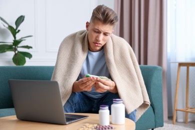 Photo of Sick man with thermometer having online consultation with doctor via laptop at home