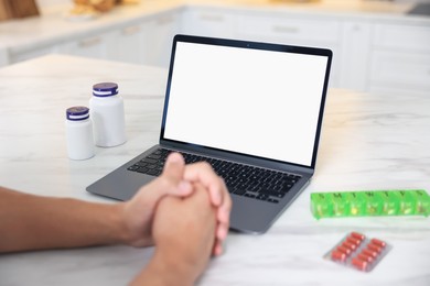 Photo of Man having online consultation with doctor via laptop at table in kitchen, closeup