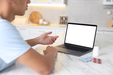 Photo of Man having online consultation with doctor via laptop at table in kitchen, closeup