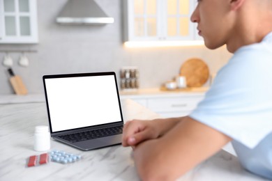 Photo of Man having online consultation with doctor via laptop at table in kitchen, closeup