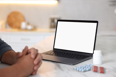 Photo of Man having online consultation with doctor via laptop at table in kitchen, closeup