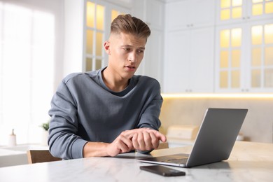 Photo of Sick man having online consultation with doctor via laptop at white marble table in kitchen
